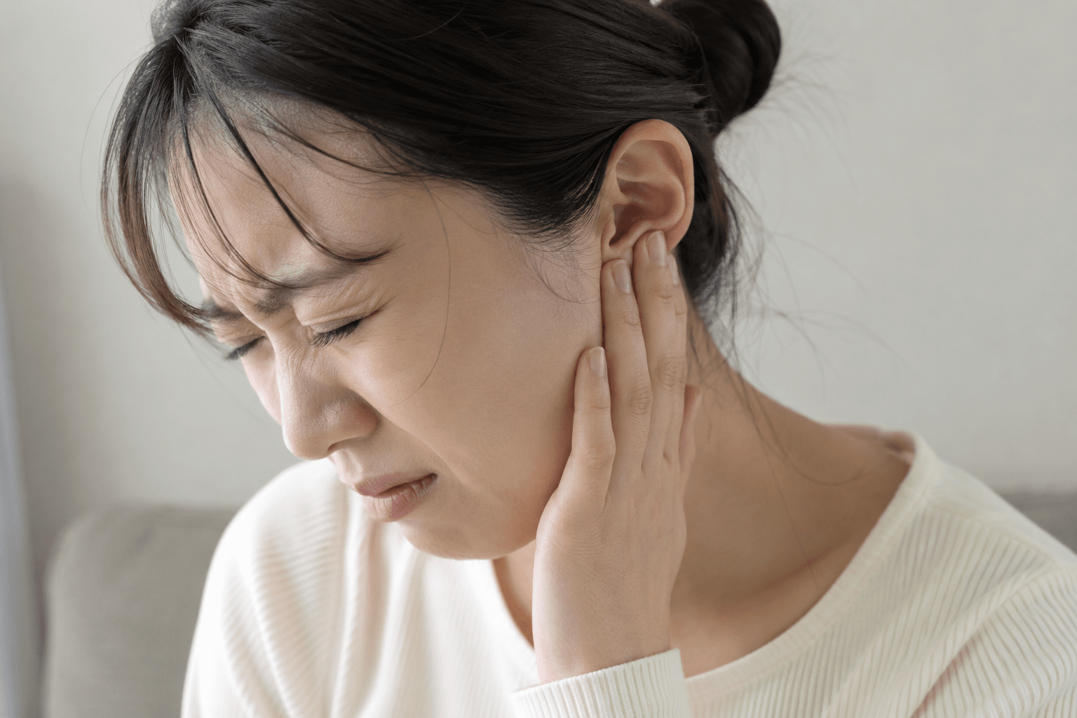 女性が片側の耳〜顎のあたりを手で押さえ、突然の強い痛みで顔をしかめている