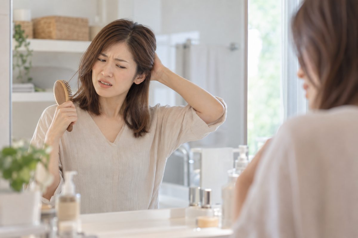 髪をとかしている途中で後頭部の痛みを感じる女性