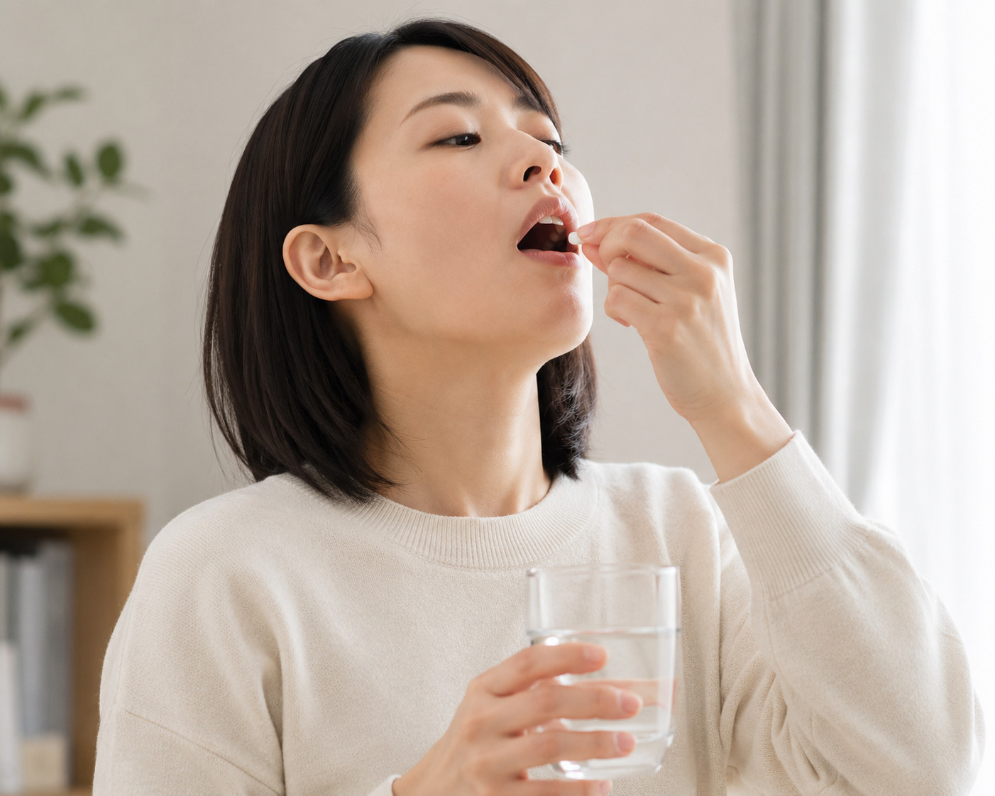水の入ったコップを手に、錠剤の薬を飲もうとする女性