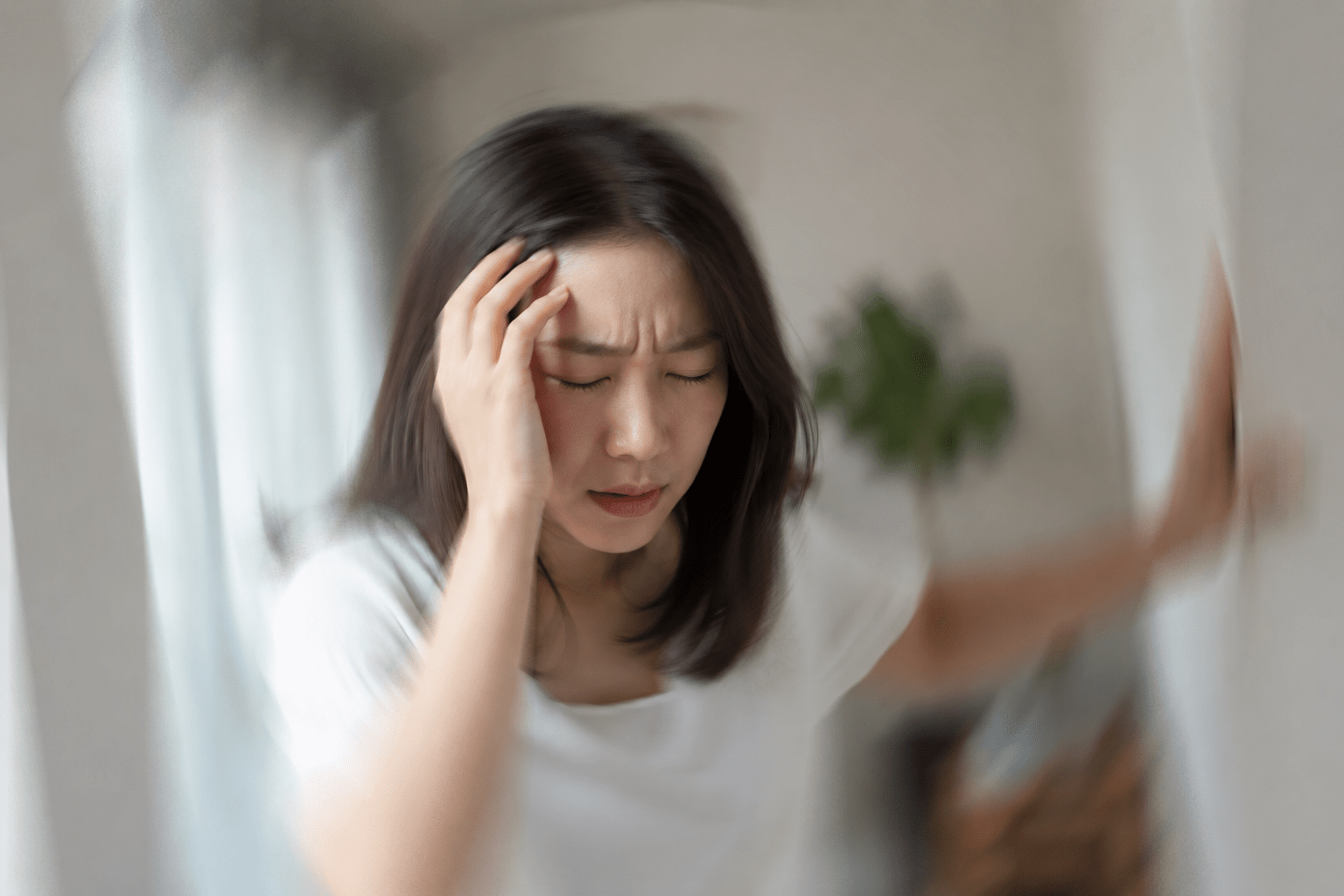 女性が両手で頭を押さえ、頭痛・めまいで苦しんでいる